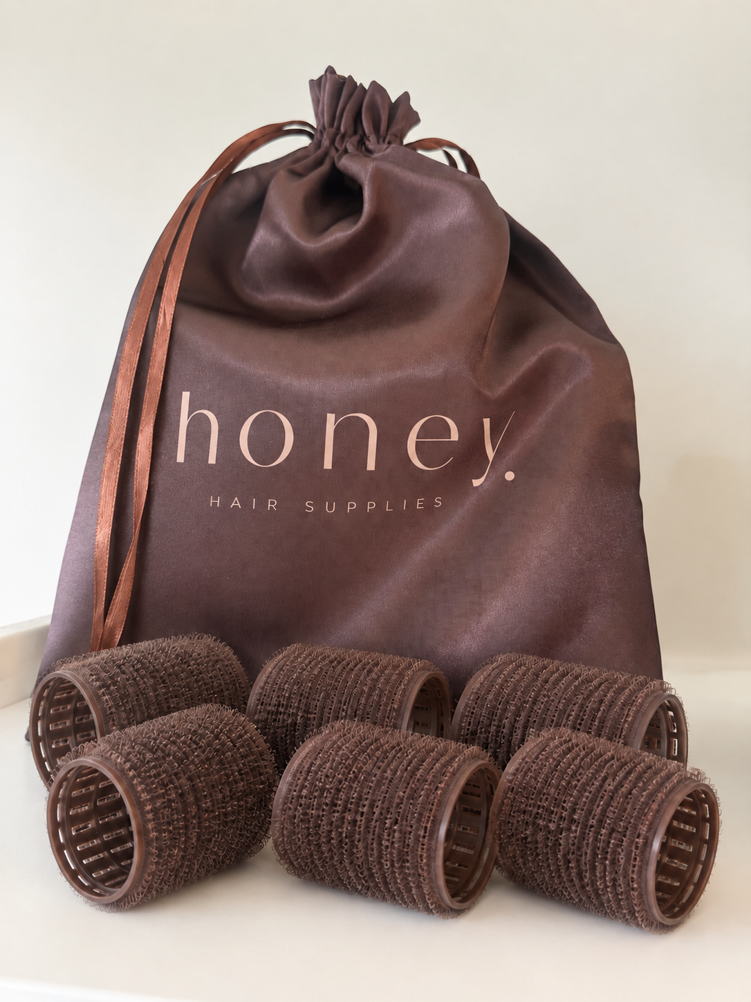 Six brunette Honey Velcro rollers with the full Honey logo visible on the satin pouch